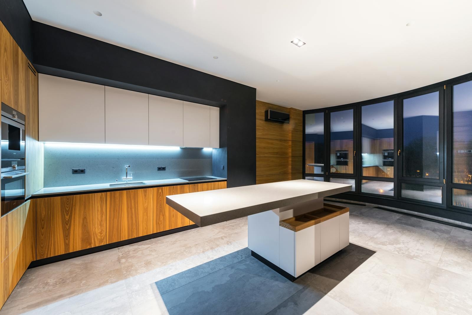 Interior of contemporary kitchen with huge windows against table and bright illumination in cooking zone